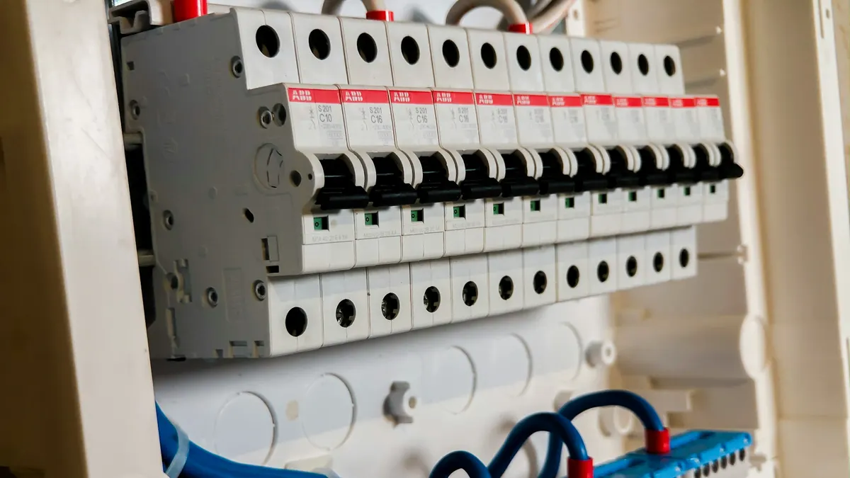 Close-up van een open groepenkast met een rij witte installatieautomaten en blauwe aansluitbedrading