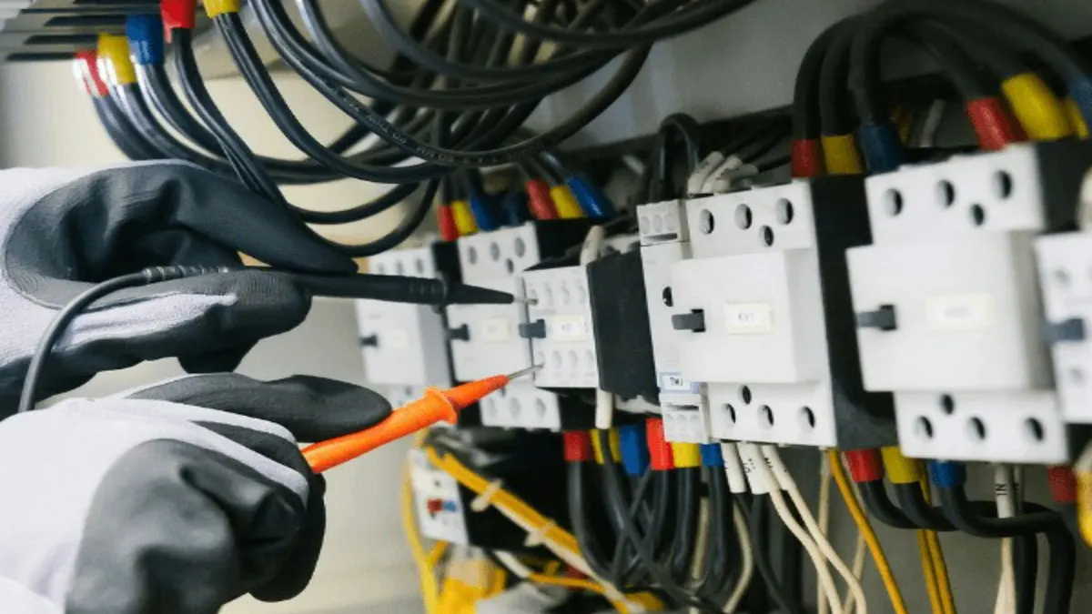 Handen in werkhandschoenen meten met de testpennen van een multimeter in een verdeelkast