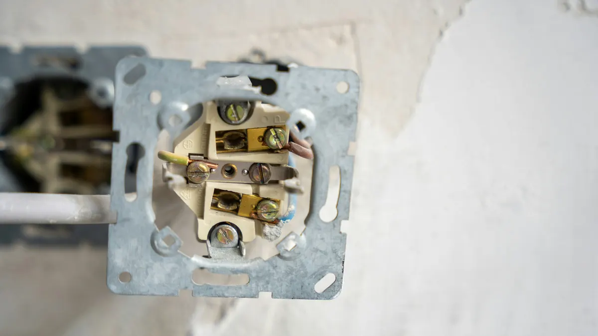Losgeschroefd inbouwstopcontact met zichtbare aansluitklemmen en draden, half uit de wandcontactdoos