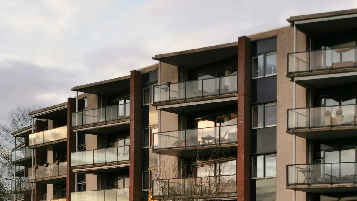 Appartementencomplex van vier verdiepingen met bakstenen gevel en balkons met glazen balustrades