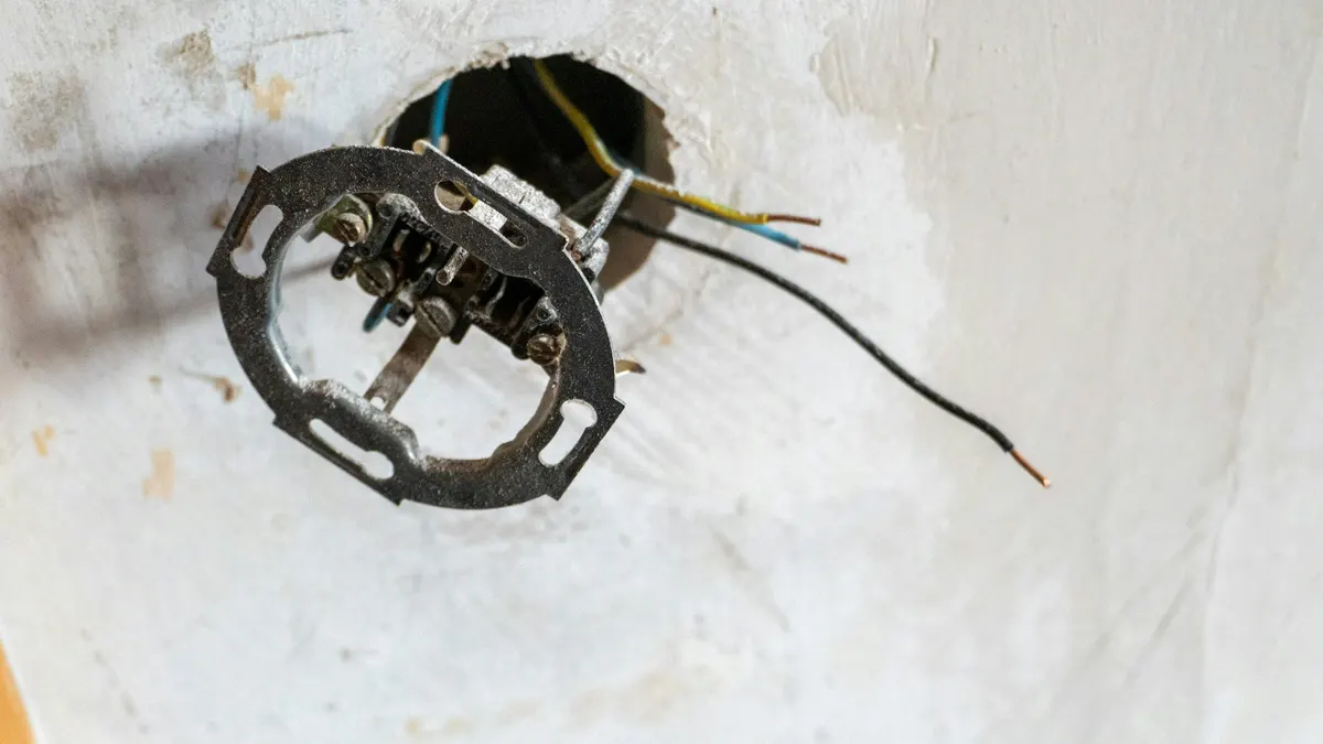 Oude losgehaalde inbouwdoos met afgeknipte draden die uit een gat in het plafond steken