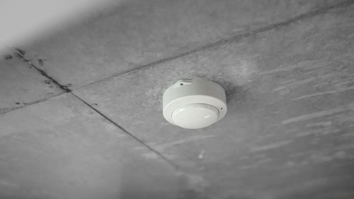 Witte rookmelder gemonteerd aan een grijs betonnen plafond, van onderaf gefotografeerd